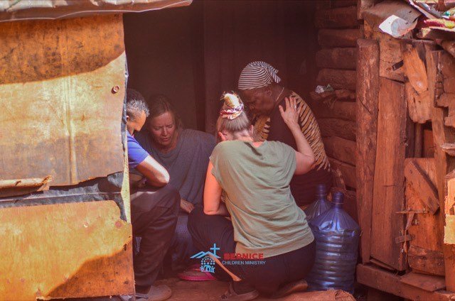 Hausbesuch in einer Hütte aus Wellblech und Holz, mehrere Menschen im Gespräch.